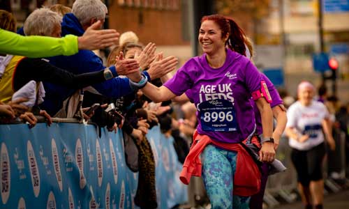 Woman giving high fives to the crowd whilst running in the ʼһ Leeds Abbey Dash